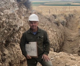 Dr. Hemphill-Haley standing in a paleoseismic trench holding a trench log and smiling